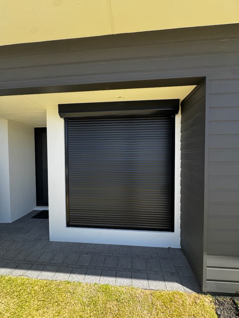 Large black roller shutter on grey weatherboard home